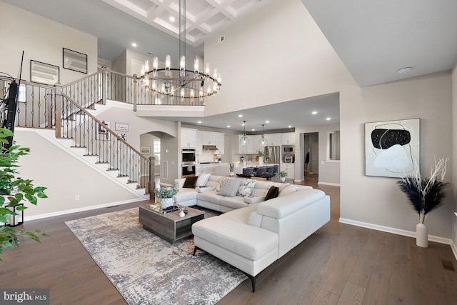 living room featuring a notable chandelier, coffered ceiling, a high ceiling, and dark hardwood / wood-style floors