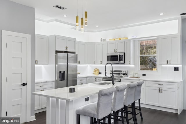 kitchen featuring a kitchen bar, a center island with sink, appliances with stainless steel finishes, dark wood-type flooring, and pendant lighting