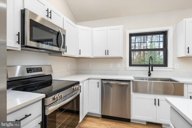 kitchen featuring vaulted ceiling, sink, light stone countertops, stainless steel appliances, and white cabinets