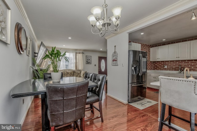 dining area featuring brick wall, ornamental molding, hardwood / wood-style flooring, and a notable chandelier