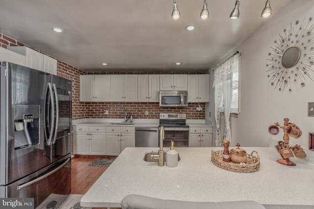 kitchen with stainless steel appliances, backsplash, brick wall, white cabinets, and sink