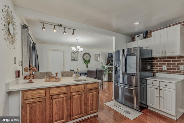 kitchen with white cabinets, stainless steel refrigerator with ice dispenser, decorative light fixtures, sink, and light hardwood / wood-style flooring