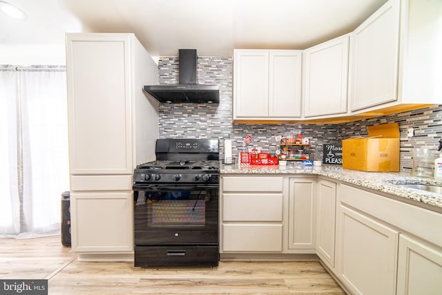 kitchen with black range with gas cooktop, tasteful backsplash, light wood-type flooring, light stone counters, and wall chimney exhaust hood