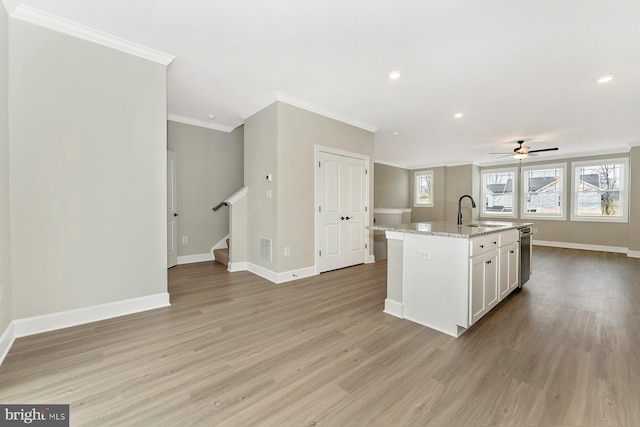 kitchen with light stone countertops, sink, ornamental molding, ceiling fan, and a center island with sink