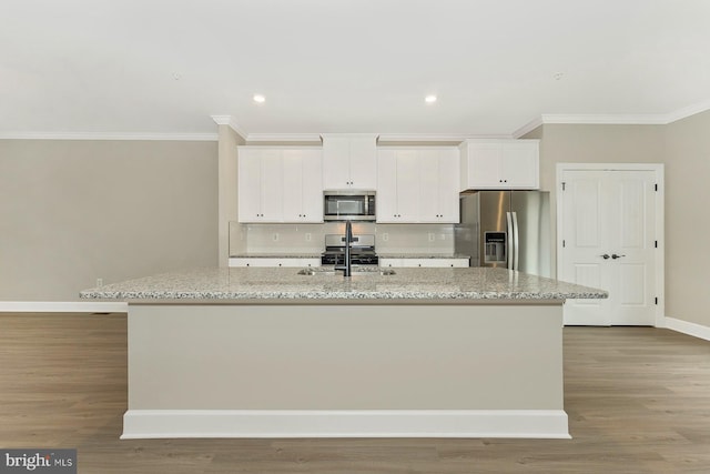 kitchen with light stone countertops, white cabinets, stainless steel appliances, and a kitchen island with sink