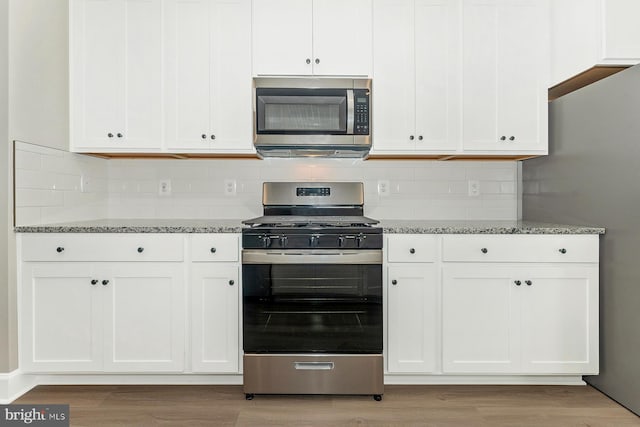 kitchen with tasteful backsplash, stone counters, white cabinetry, light wood-type flooring, and stainless steel appliances