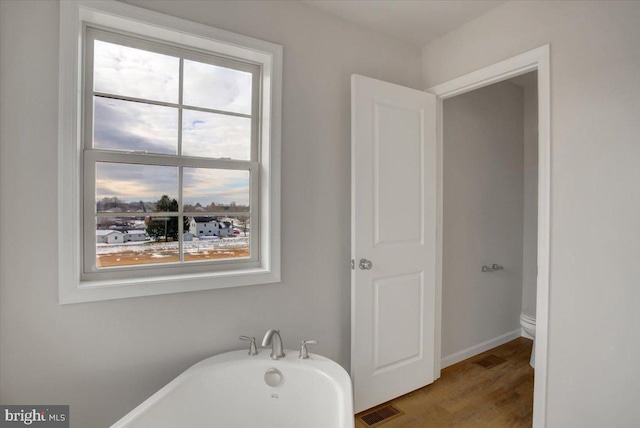 bathroom with toilet, a bathtub, and wood-type flooring