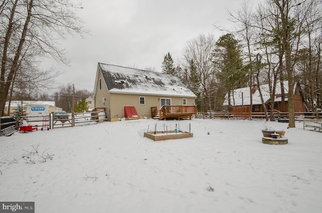 snow covered back of property with a deck and a fire pit