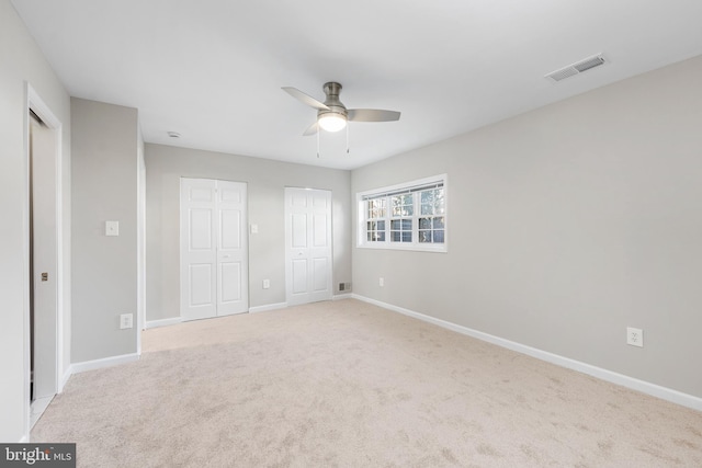 unfurnished bedroom with two closets, light colored carpet, and ceiling fan