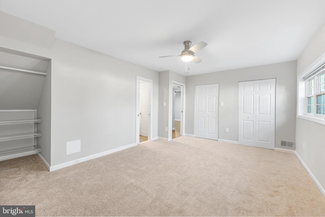 unfurnished bedroom with multiple closets, light colored carpet, and ceiling fan