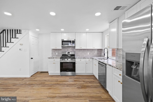 kitchen with light stone counters, white cabinetry, appliances with stainless steel finishes, and light hardwood / wood-style flooring