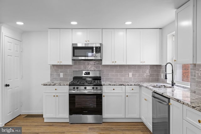 kitchen featuring white cabinets, appliances with stainless steel finishes, wood-type flooring, sink, and backsplash