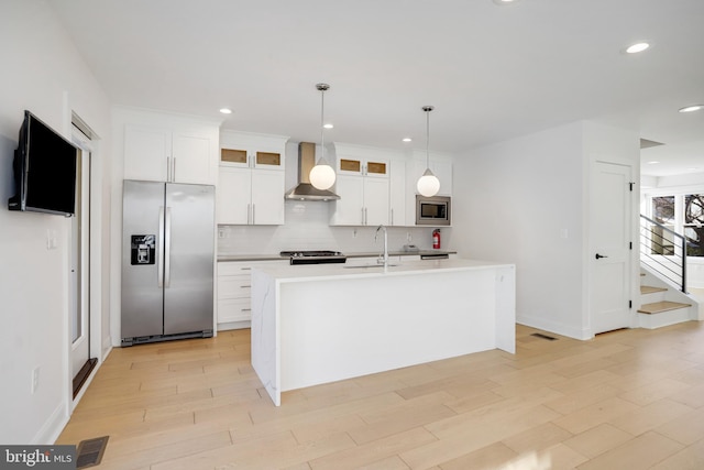 kitchen with an island with sink, wall chimney range hood, white cabinetry, and stainless steel appliances