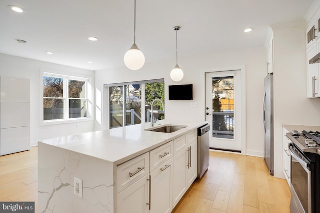 kitchen featuring a center island with sink, stainless steel appliances, white cabinets, pendant lighting, and sink