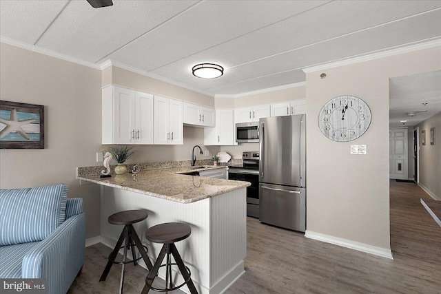 kitchen featuring appliances with stainless steel finishes, a breakfast bar, sink, white cabinets, and kitchen peninsula