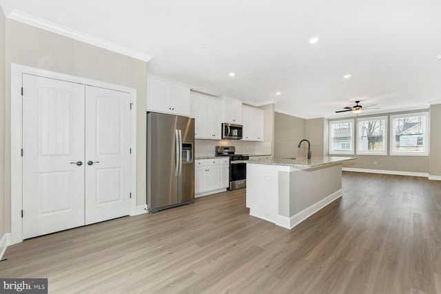 kitchen featuring white cabinets, stainless steel appliances, ceiling fan, light stone counters, and a center island with sink