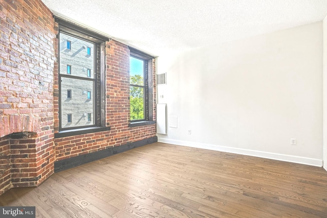 spare room featuring hardwood / wood-style flooring, brick wall, and a textured ceiling