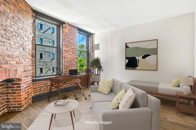 living room with a fireplace, brick wall, wood-type flooring, and a textured ceiling