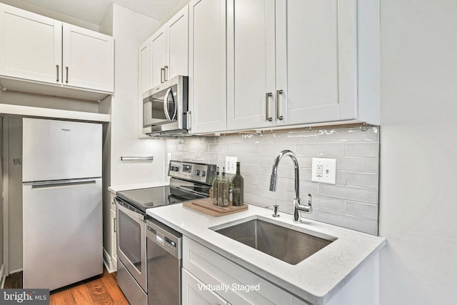 kitchen with sink, light stone counters, stainless steel appliances, white cabinets, and hardwood / wood-style flooring