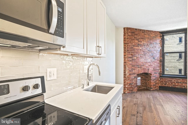 kitchen featuring appliances with stainless steel finishes, sink, dark hardwood / wood-style floors, brick wall, and white cabinets