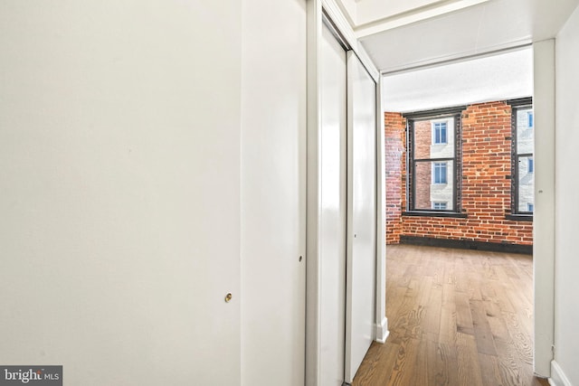 corridor featuring brick wall and wood-type flooring