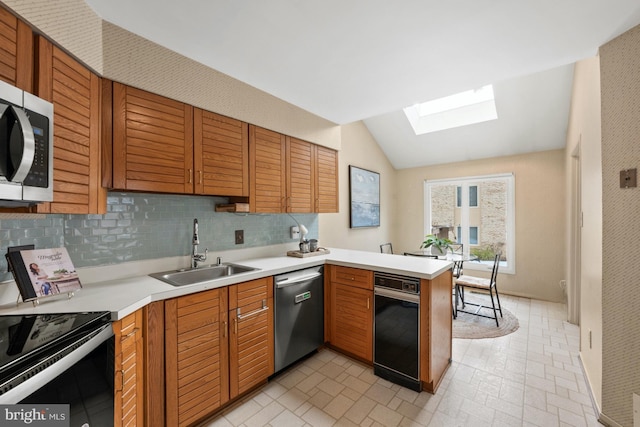 kitchen featuring tasteful backsplash, vaulted ceiling with skylight, kitchen peninsula, sink, and appliances with stainless steel finishes