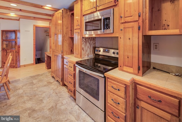 kitchen featuring stainless steel appliances, beamed ceiling, tile counters, and decorative backsplash