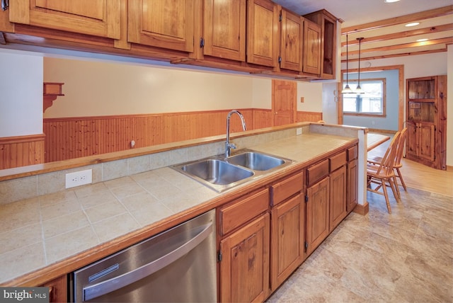 kitchen with tile counters, dishwasher, hanging light fixtures, wooden walls, and sink