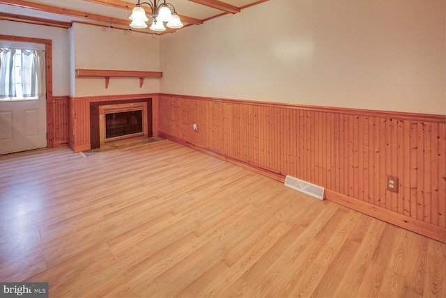 unfurnished living room with an inviting chandelier, light hardwood / wood-style flooring, and beamed ceiling