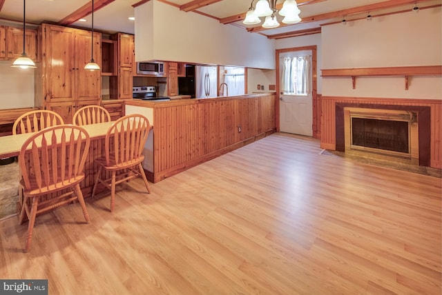 kitchen featuring light wood-type flooring, decorative light fixtures, beam ceiling, kitchen peninsula, and stainless steel appliances