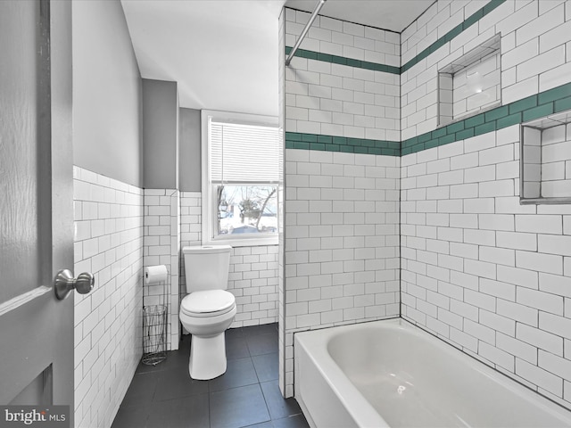 bathroom featuring tile patterned floors, toilet, tile walls, and washtub / shower combination