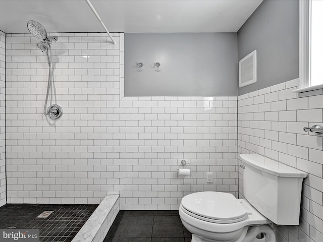 bathroom featuring a tile shower, toilet, tile patterned floors, and tile walls