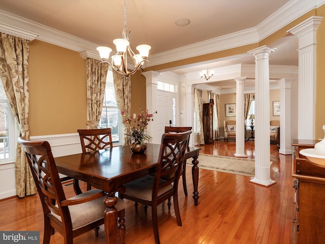 dining room featuring crown molding, a notable chandelier, wood-type flooring, and ornate columns