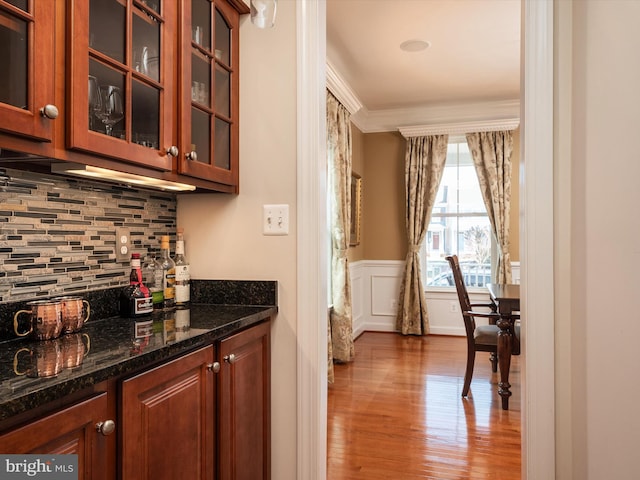 bar with dark stone countertops, crown molding, light hardwood / wood-style flooring, and tasteful backsplash