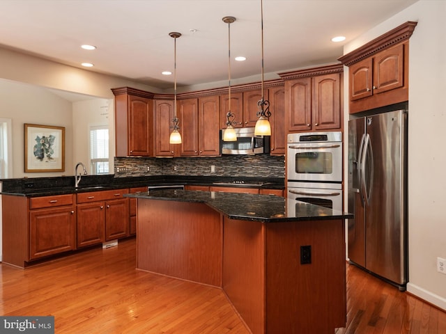 kitchen with pendant lighting, stainless steel appliances, a kitchen island, and dark stone counters