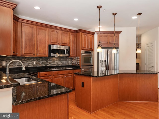 kitchen with pendant lighting, sink, dark stone countertops, stainless steel appliances, and a kitchen island