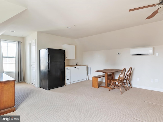 kitchen featuring an AC wall unit, black refrigerator, lofted ceiling, white cabinets, and light colored carpet