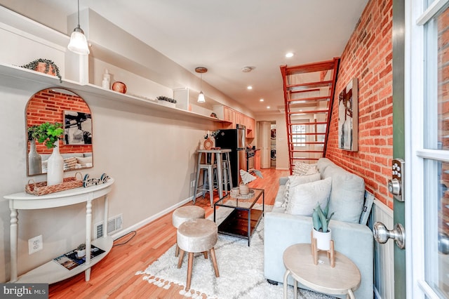 living room with stacked washer / dryer, brick wall, and light hardwood / wood-style flooring