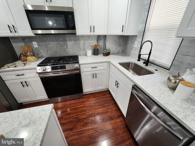 kitchen with appliances with stainless steel finishes, sink, light stone counters, and white cabinetry