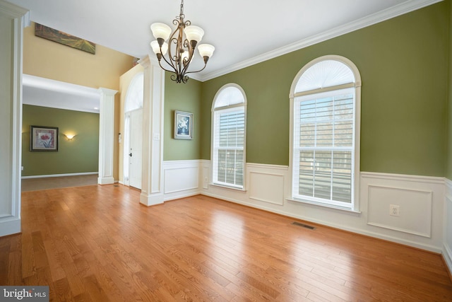 unfurnished dining area featuring a wainscoted wall, decorative columns, a notable chandelier, visible vents, and wood finished floors