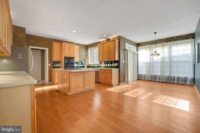 kitchen featuring light brown cabinets, light countertops, appliances with stainless steel finishes, light wood-type flooring, and a center island