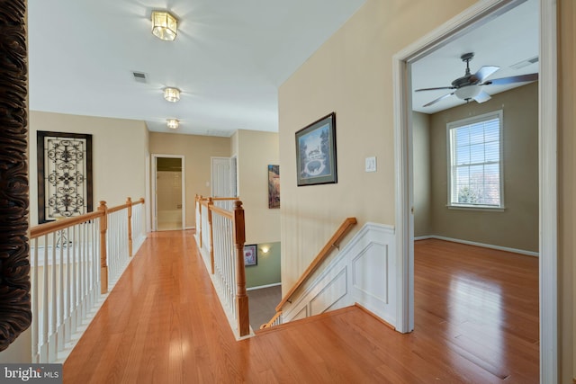 hallway with baseboards, visible vents, light wood-style flooring, and an upstairs landing