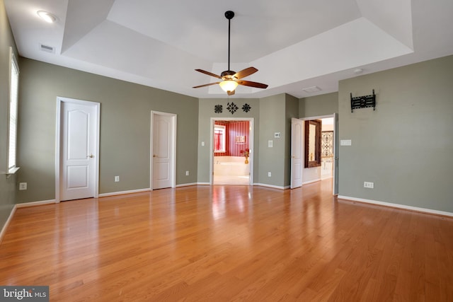 interior space with light wood-type flooring, baseboards, a raised ceiling, and a ceiling fan