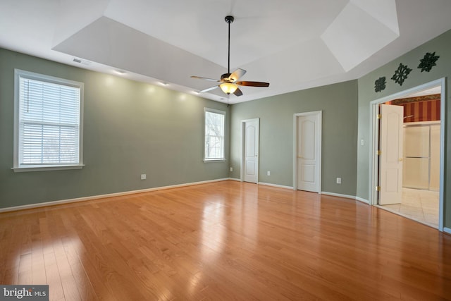 interior space with light wood-style floors, baseboards, visible vents, and a raised ceiling