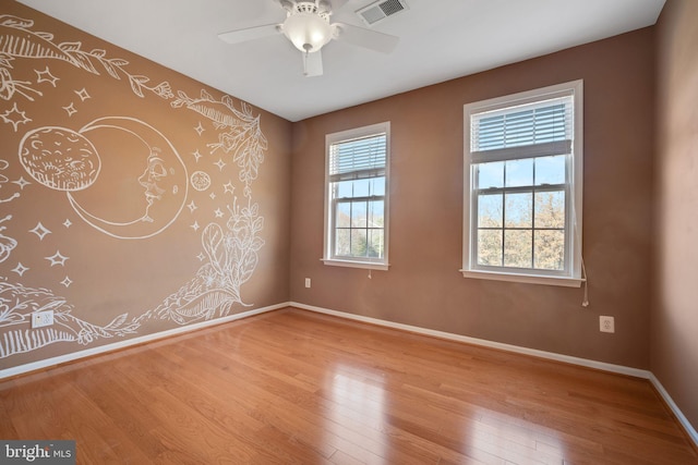 empty room featuring a ceiling fan, baseboards, visible vents, and light wood finished floors