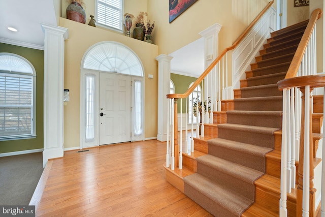 entrance foyer featuring decorative columns, baseboards, a towering ceiling, light wood-style flooring, and ornamental molding