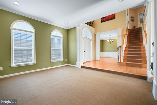 carpeted spare room with decorative columns, visible vents, ornamental molding, an inviting chandelier, and stairs