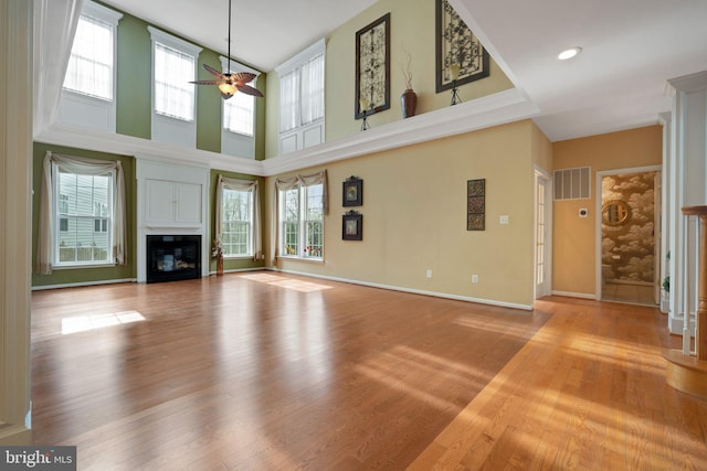 unfurnished living room with ceiling fan, wood finished floors, a glass covered fireplace, and visible vents