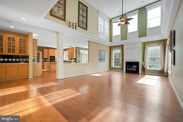 unfurnished living room featuring light wood finished floors, a glass covered fireplace, decorative columns, and a ceiling fan