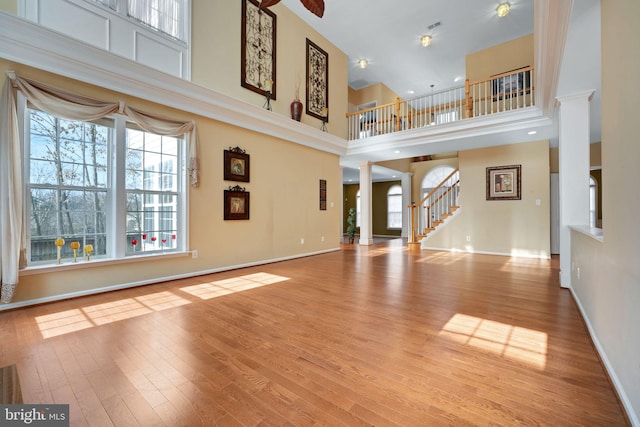 unfurnished living room with baseboards, a towering ceiling, wood finished floors, stairs, and ornate columns